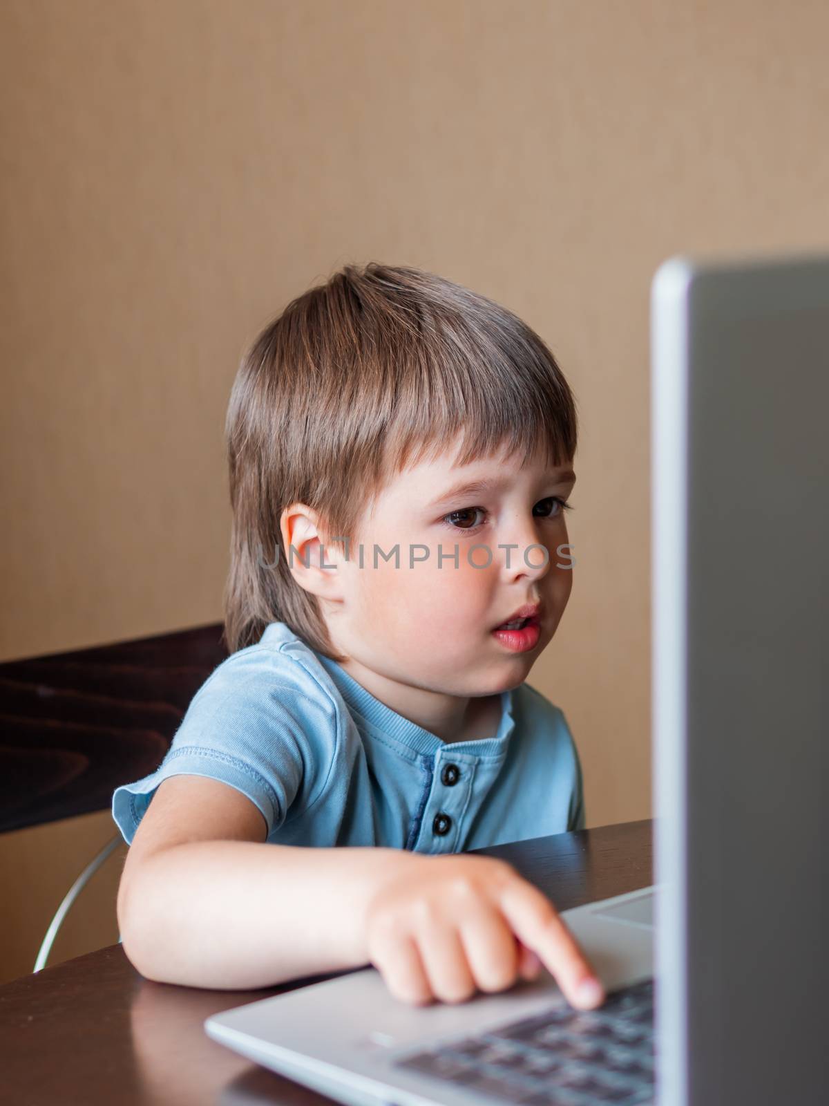 Curious toddler boy explores the laptop and presses buttons on computer keyboard. Online education for babies.