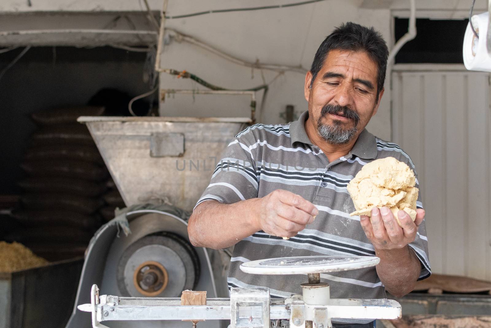 man selling dough in nixtamal mill. A pendulum scale is being used to weigh the dough.