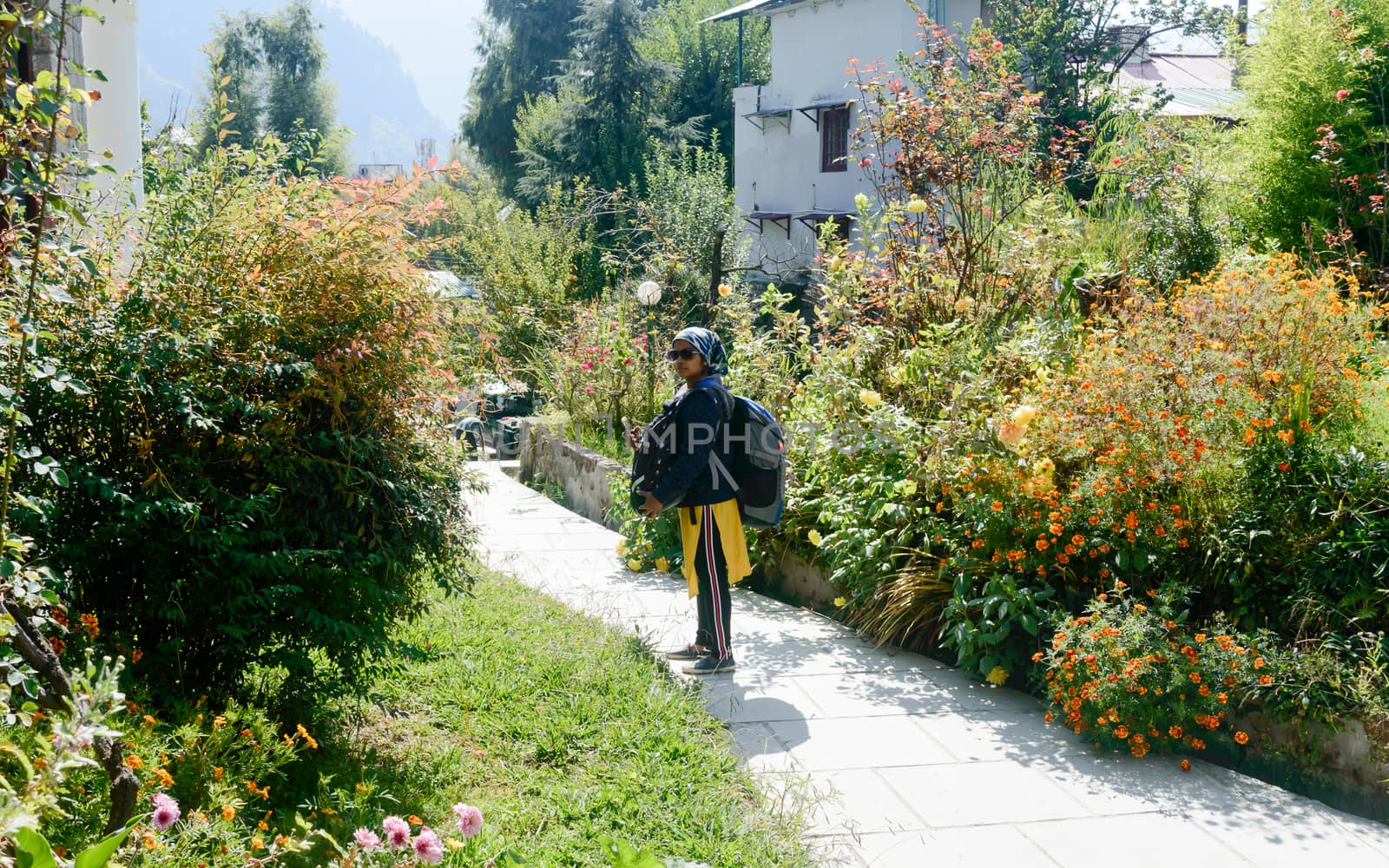 Front View solo woman in hiking sportswear and with a backpack on her shoulders. Sporty woman with backpack walking outdoors. Travel girl stands on garden front yard and looking at camera. Adventure Sports Healthy lifestyle background. by sudiptabhowmick