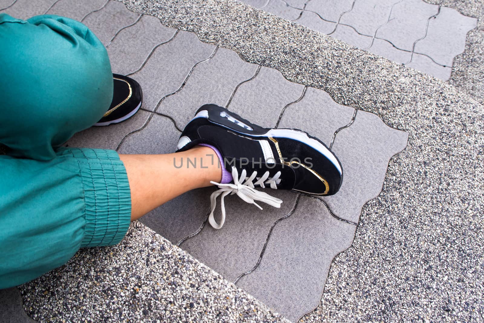 The legs and shoes of a girl sitting on the concrete steps by Satakorn