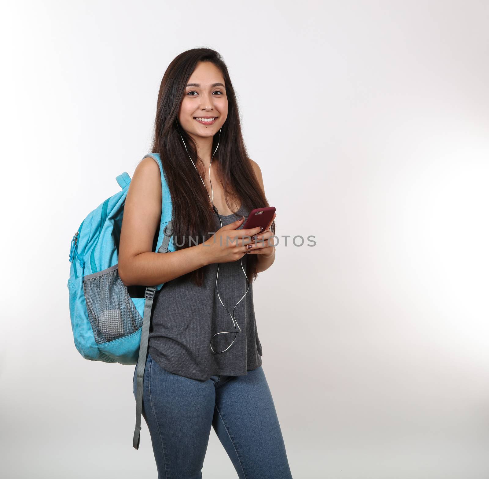 A pretty female student is listening to music on her phone while wearing a backpack.