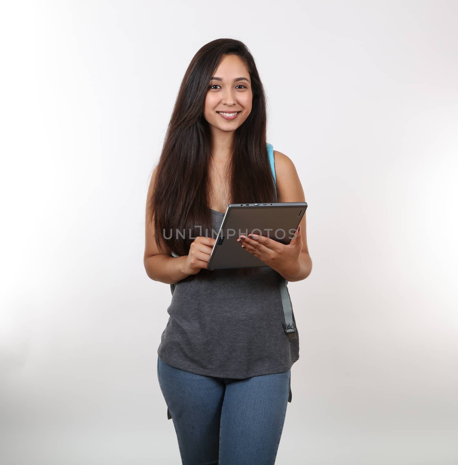 An attractive student smiles wearing backpack as she uses her tablet.