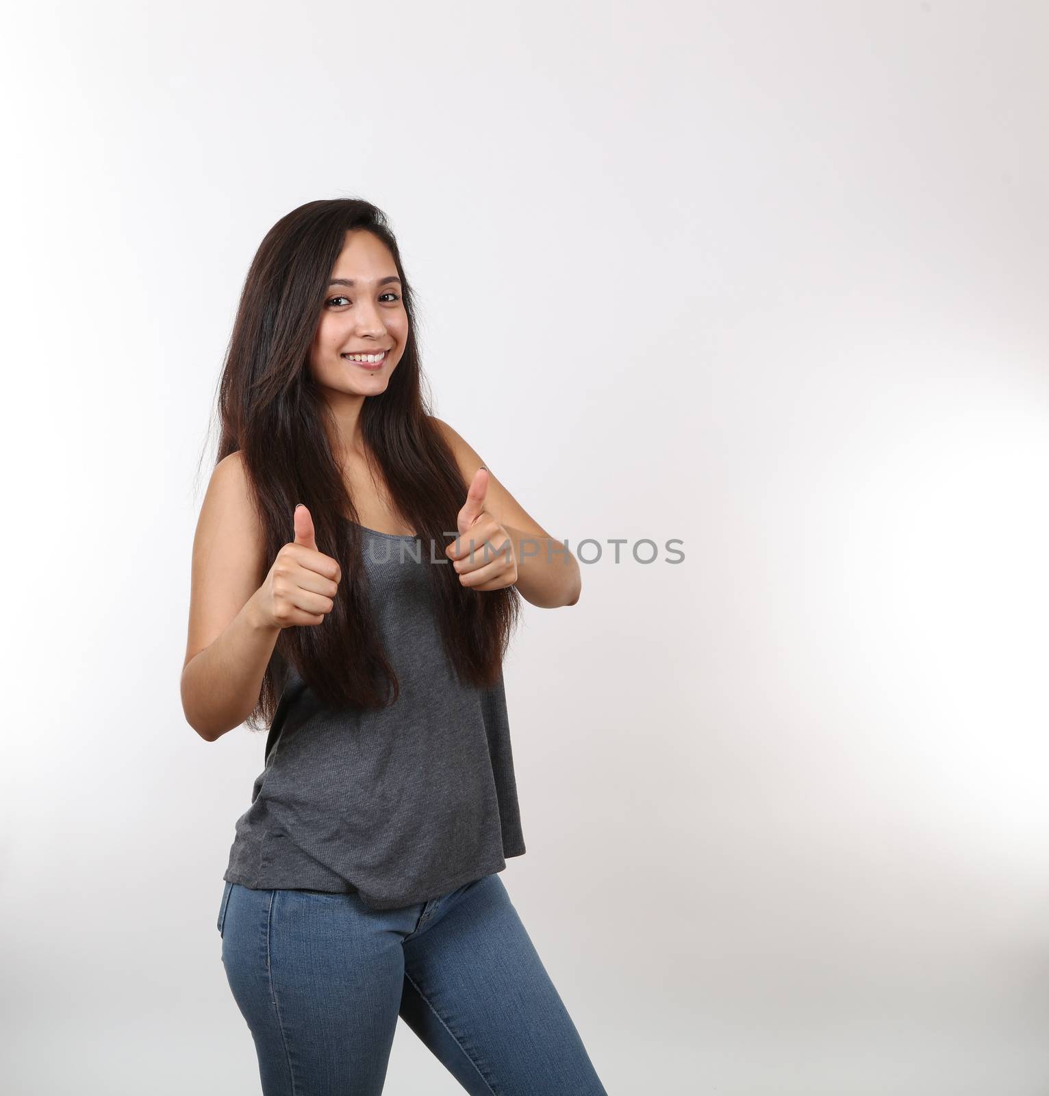 A young attractive girl wearing jeans gives two thumbs up.