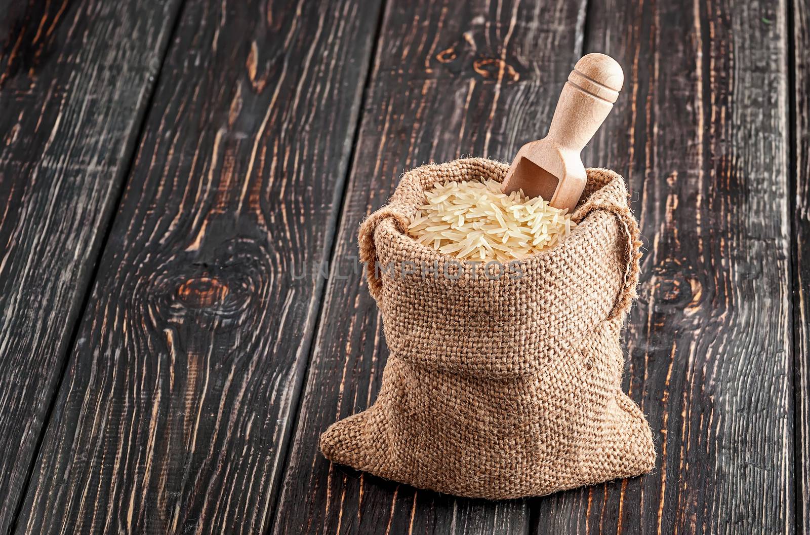Sack with long rice and spoon stands on wooden background