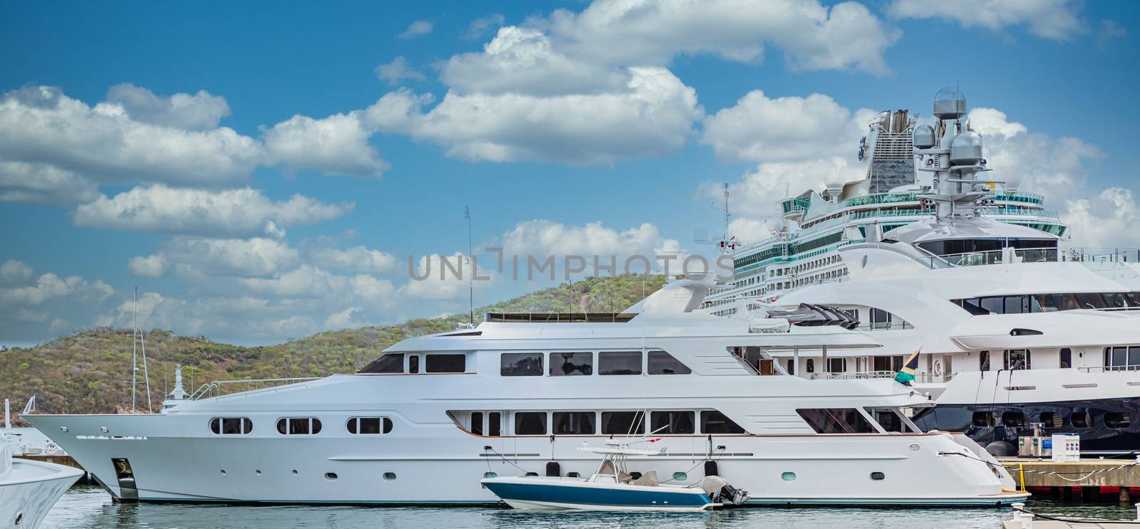 A small blue and white boat by a massive luxury yacht in front of a cruise ship