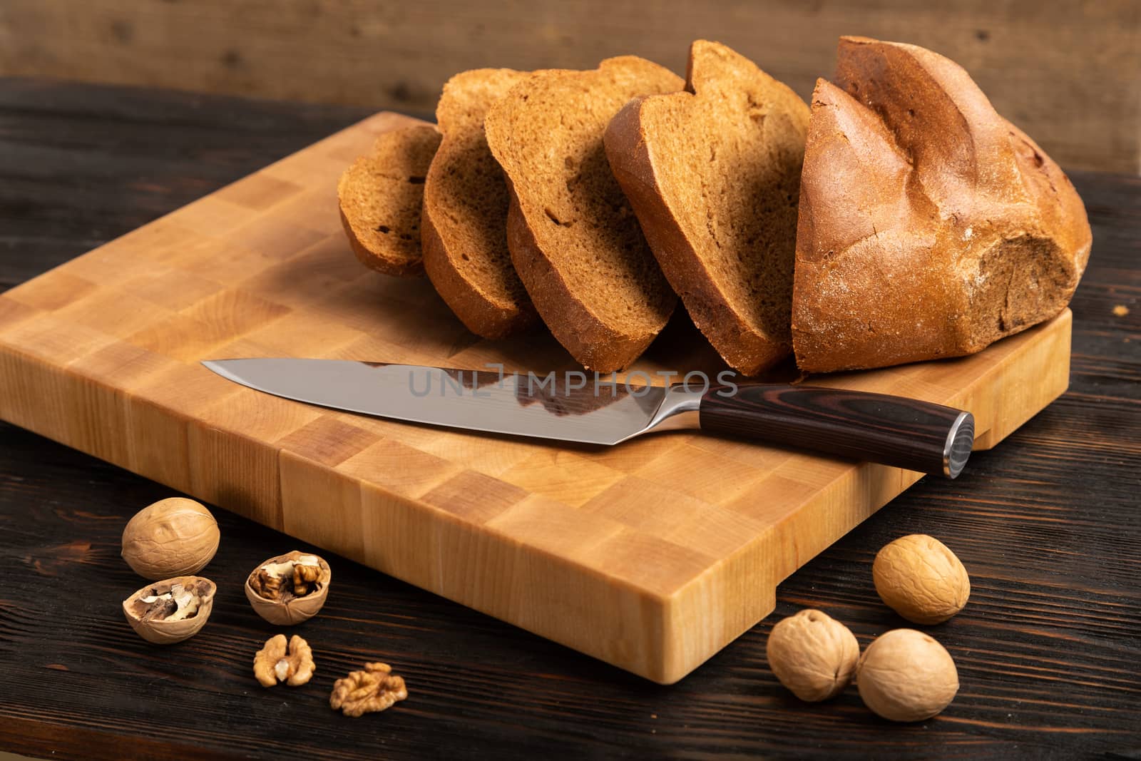 A loaf of bread sliced into slices with a knife on a wooden cutting board