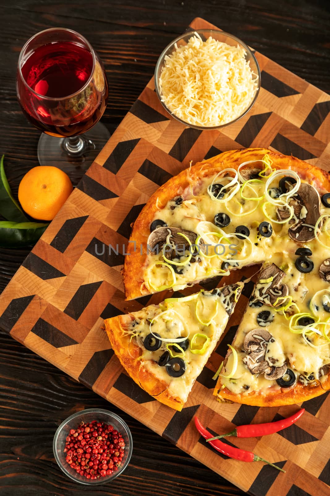 Pizza on a wooden cutting board next to vegetables, spices and a glass of wine