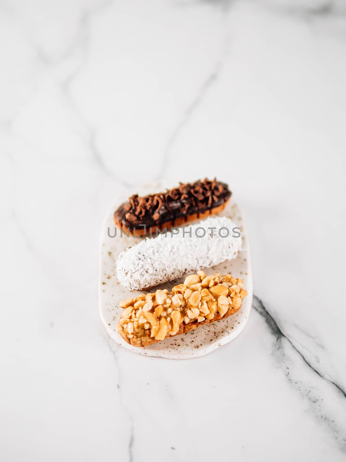 Set of three homemade eclairs on marble background. Top view of delicious healthy profitroles with different decor elements - chocolate, peanut and sherdded coconut. Vertical