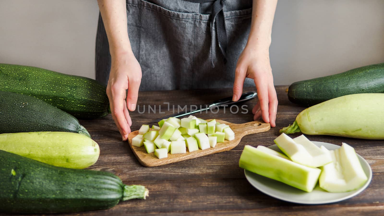 Zucchini harvest. Woman slices zucchini cubes for freezing on wooden table. Farm organic zucchini harvesting