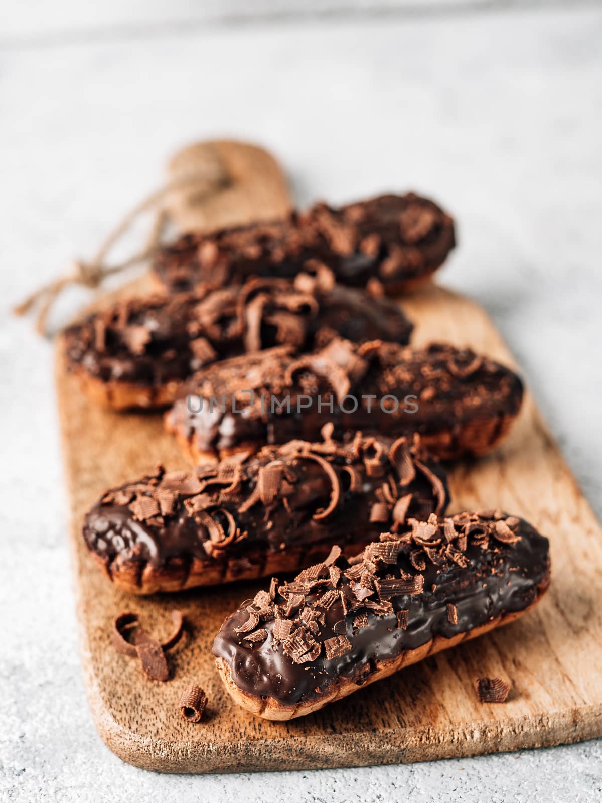 Homemade eclairs with chocolate on wooden cutting board. Close up view of delicious healthy profitroles with chocolate glaze. Copy space for text or design. Vertical.