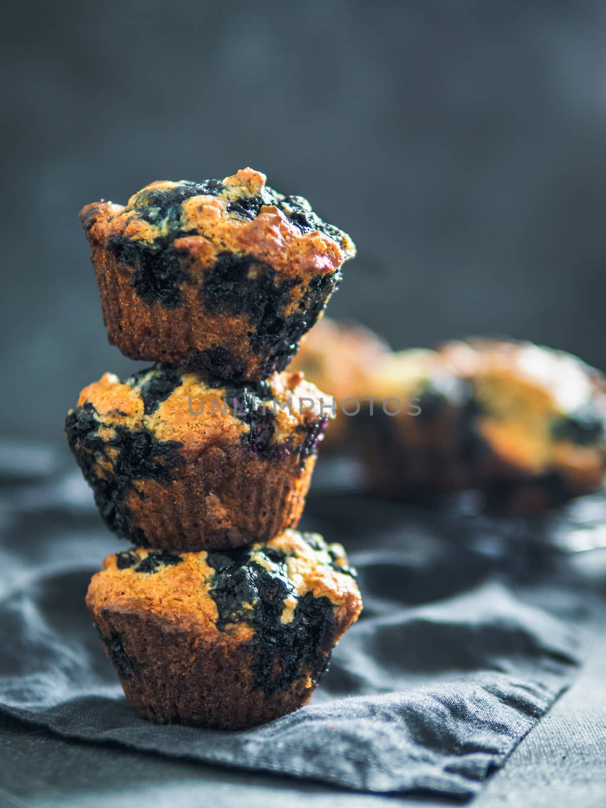 Homemade vegan blueberry muffins on dark background. Stack of three egg-free muffins with copy space for text or design. Low key. Vertical.