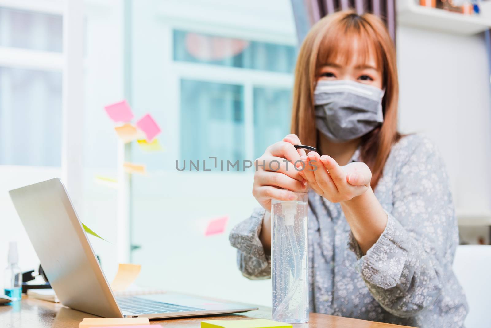 Asian young business woman wearing face mask protective working from home office with laptop computer he quarantines disease coronavirus or COVID-19 and cleaning hands with sanitizer alcohol gel pump