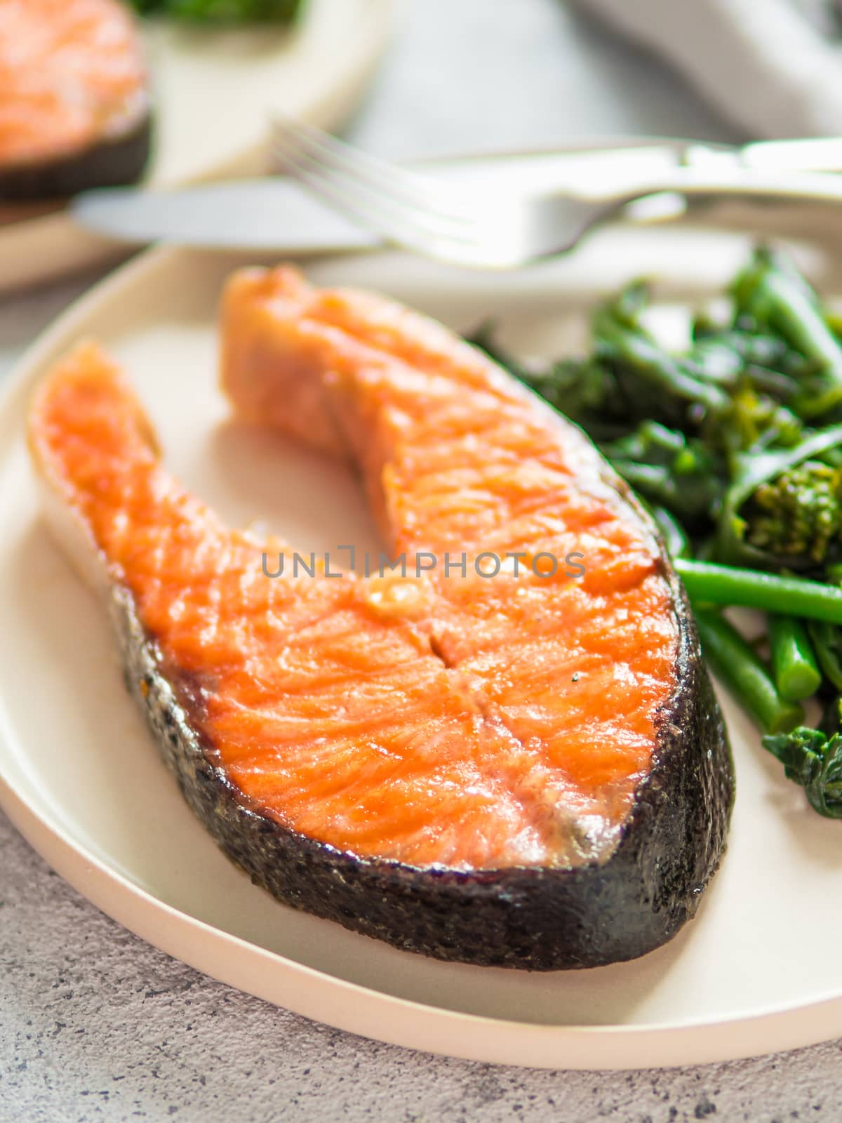 Ready-to-eat grilled salmon steak and greens - baby broccoli or broccolini and spinach on rustic craft plate over gray background. Keto diet dish.