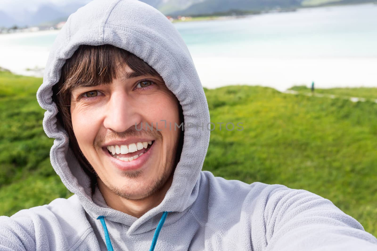 Tourist man making selfie on Rambergstranda beach on Lofoten islands. Beautiful sandy beach and azure water. Norway.