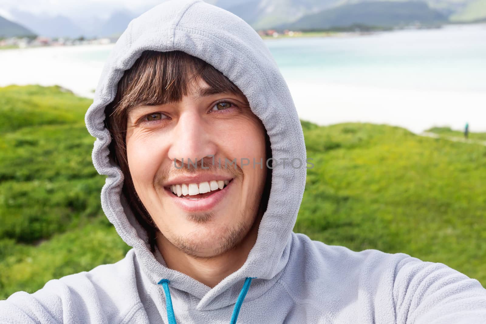 Tourist man making selfie on Rambergstranda beach on Lofoten islands. Beautiful sandy beach and azure water. Norway.