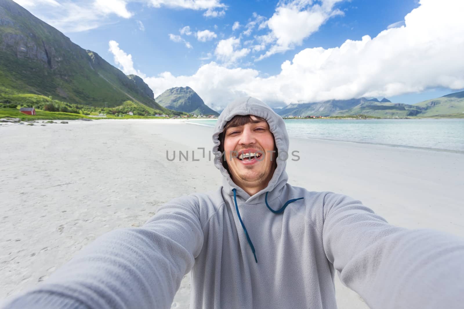 Tourist man making selfie on Rambergstranda beach on Lofoten islands. Beautiful sandy beach and azure water. Norway.