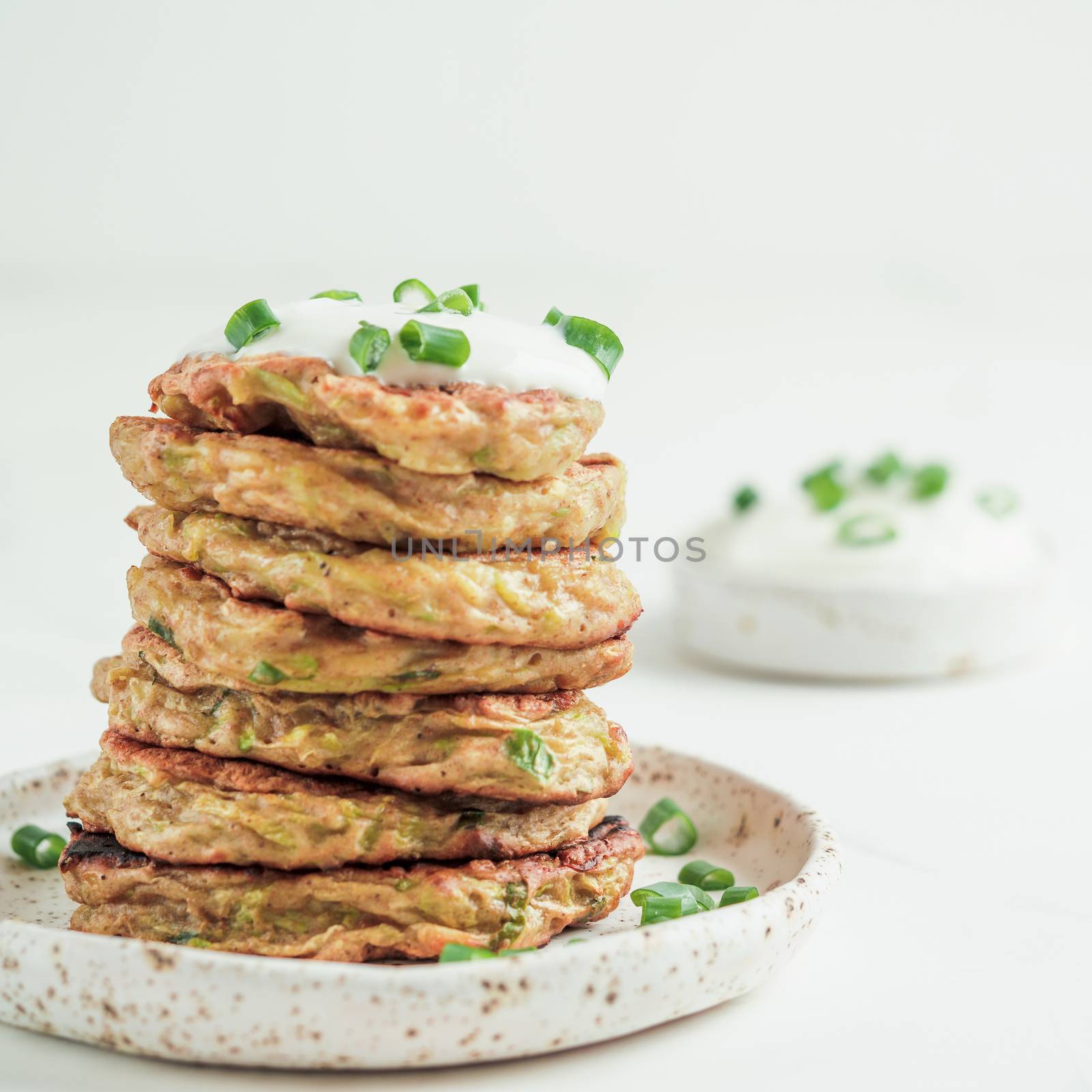 Zucchini fritters. Traditional zucchini fritters in stack on white background. Zucchini pancakes or fritters with green onion and parmesan cheese,served sour cream or greek yogurt. Copy space for text