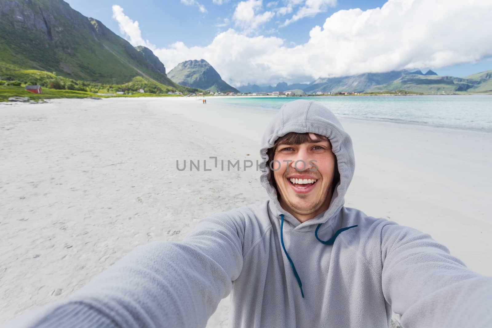 Tourist man making selfie on Rambergstranda beach on Lofoten islands. Beautiful sandy beach and azure water. Norway.