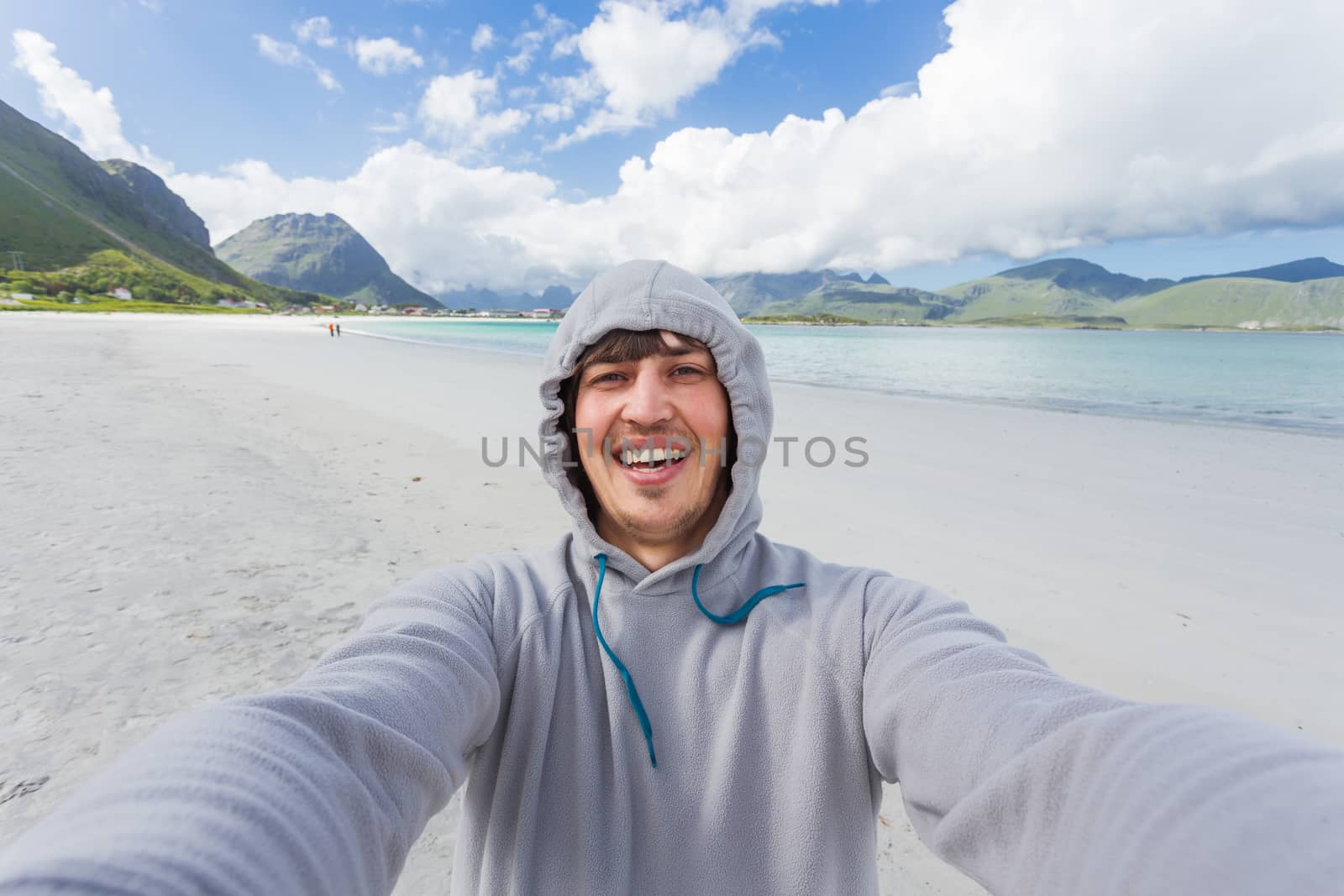 Tourist man making selfie on Rambergstranda beach on Lofoten islands. Beautiful sandy beach and azure water. Norway.