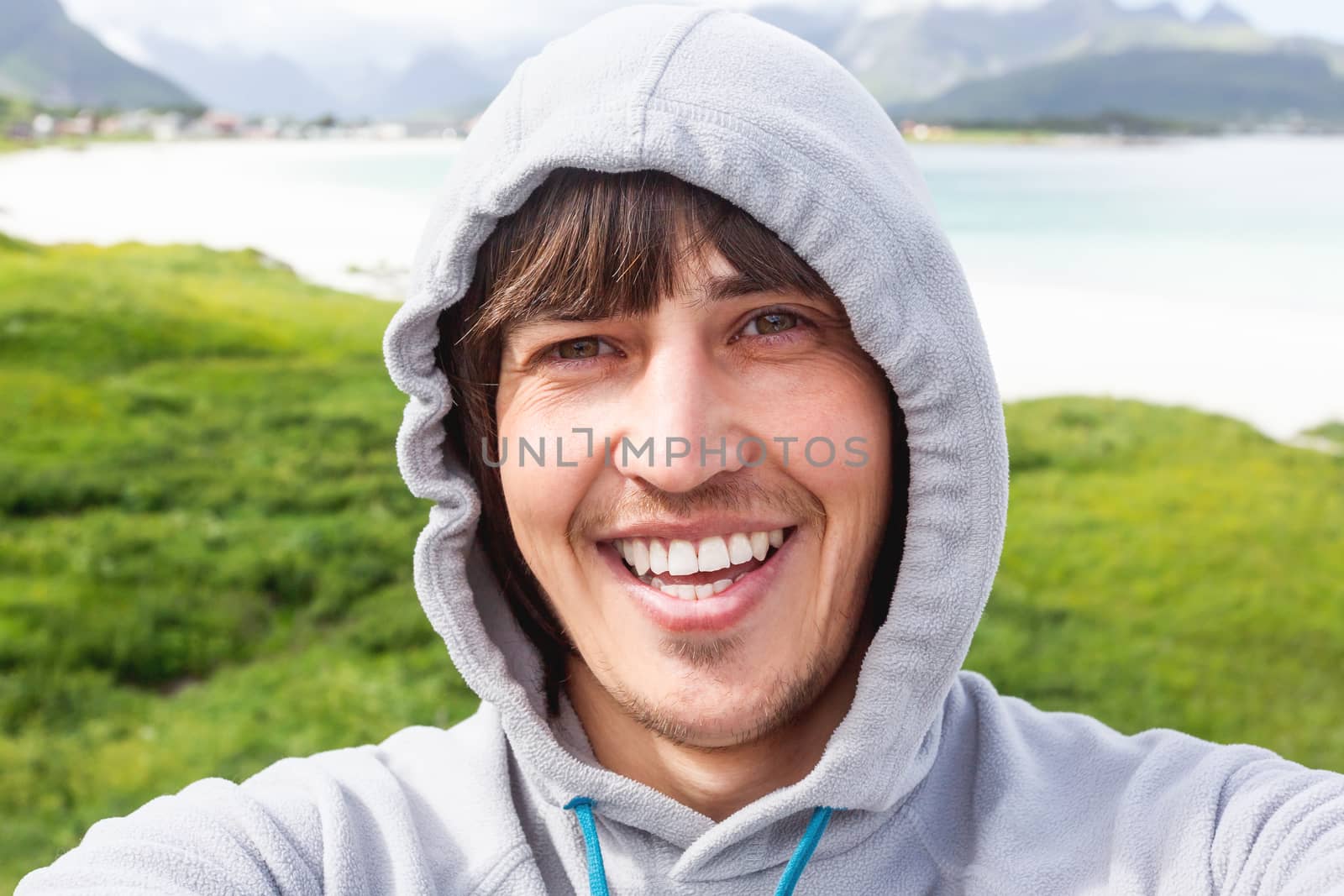 Tourist man making selfie on Rambergstranda beach on Lofoten islands. Beautiful sandy beach and azure water. Norway.