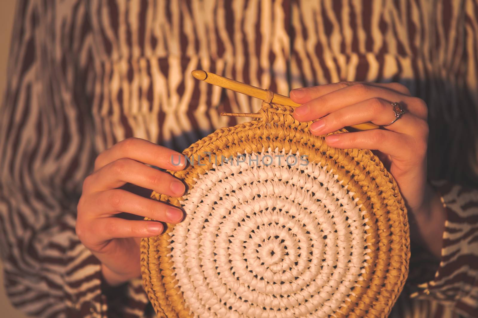 Round raffia crochet panno in female hands. Handcraft, hobby concept: holding a wall hanging and a crochet hook