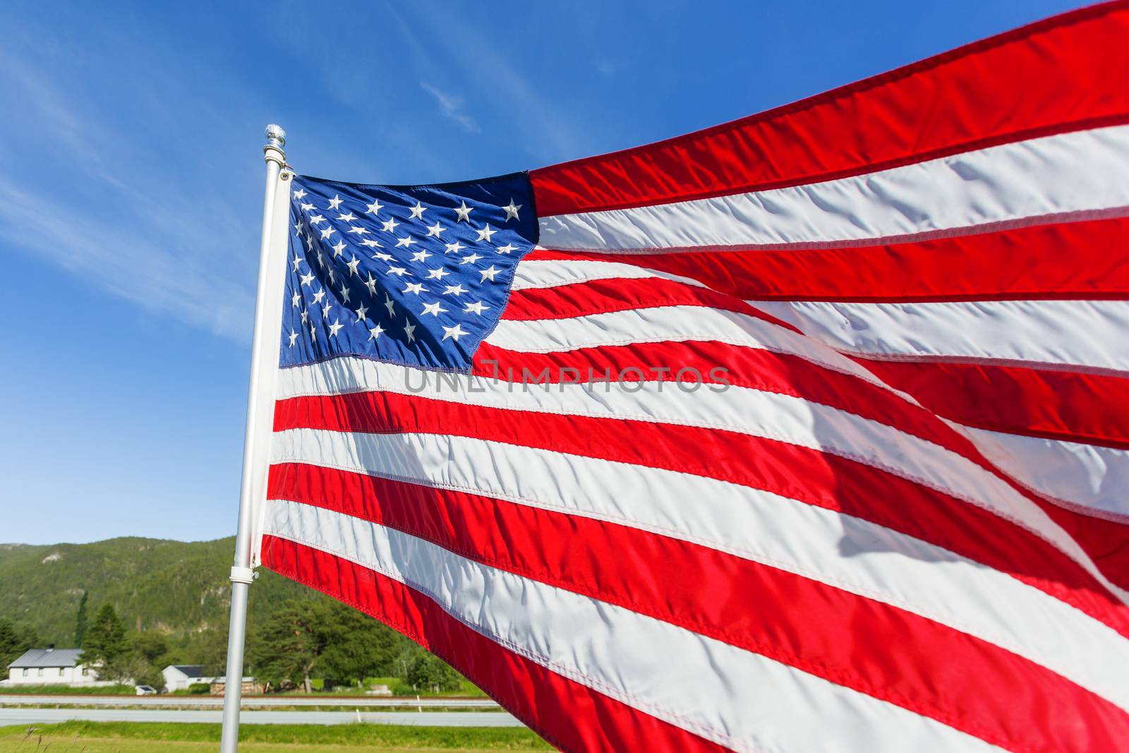 Flag of the United States of America (American flag or The Stars and Stripes, Old Glory, The Star-Spangled Banner) waving in the wind against summer forest landscape in sunny day.