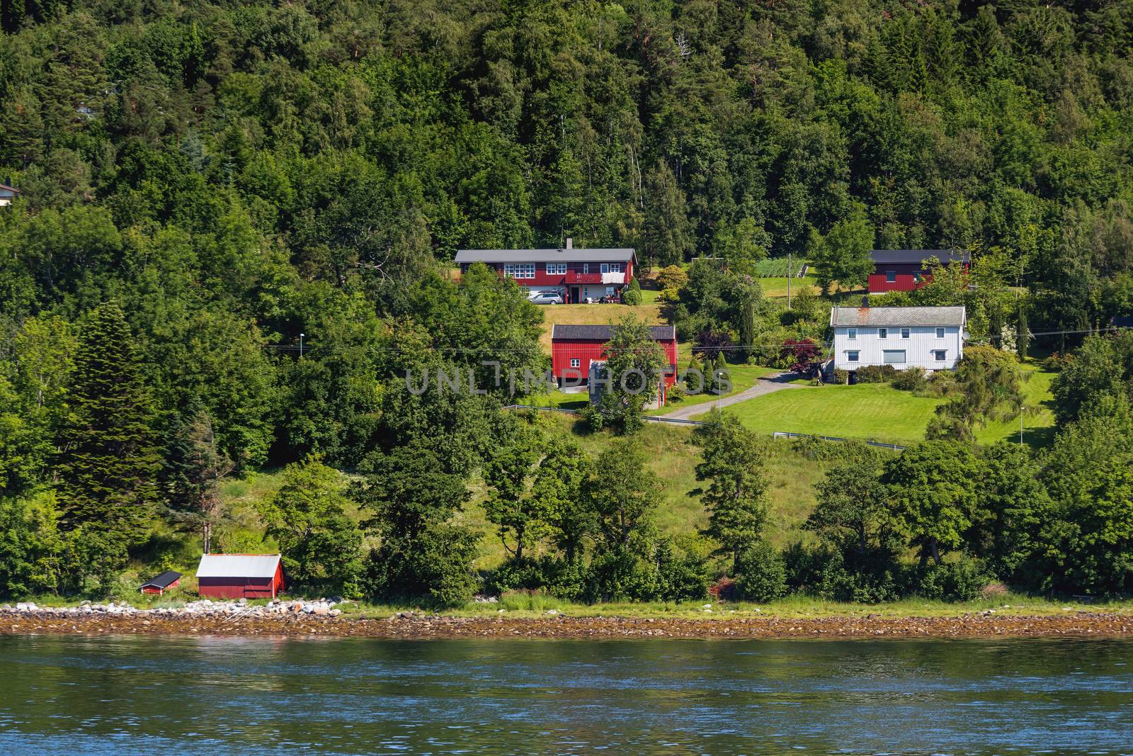 Typical scandinavian landscape with meadows and village. Houses with red walls and roofs, lawns. Norway.