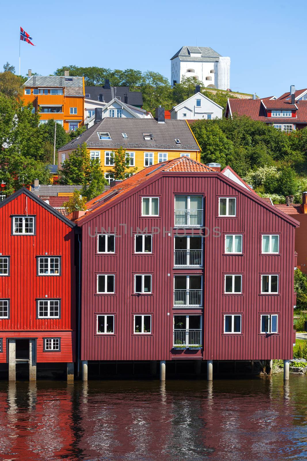 Famous wooden colored houses in Trondheim city, Norway. Colorful houses on stilts and flag of Norway in sunny day.