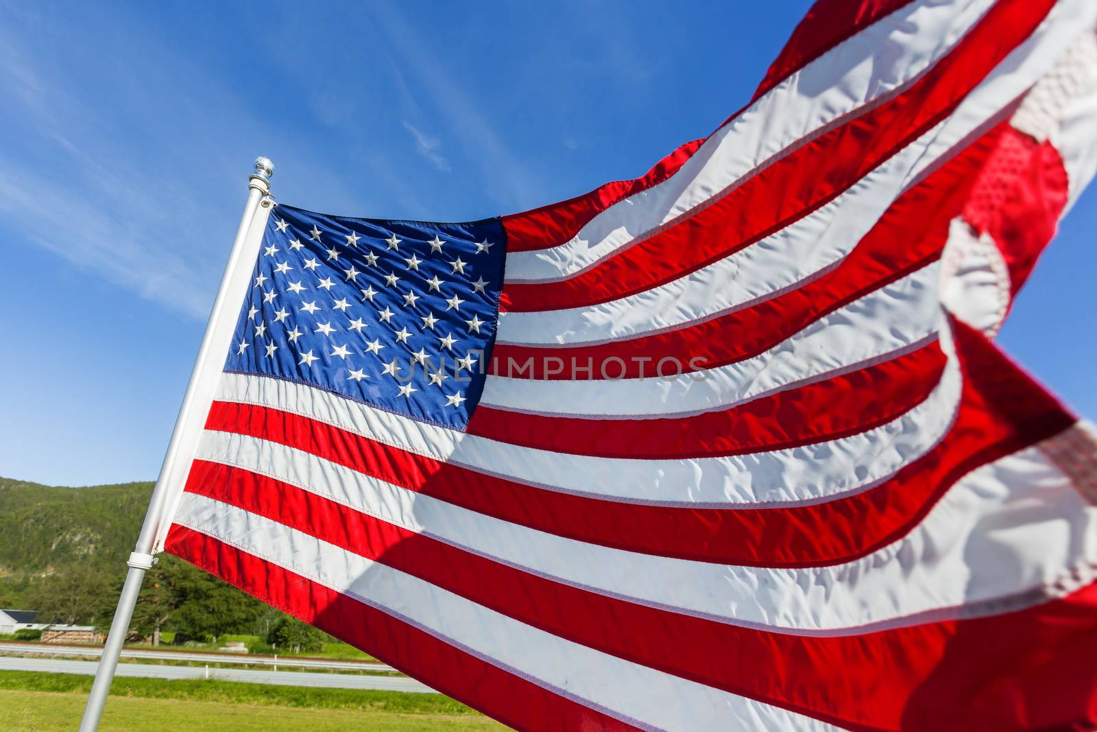 Flag of the United States of America (American flag or The Stars and Stripes, Old Glory, The Star-Spangled Banner) waving in the wind against summer forest landscape in sunny day.