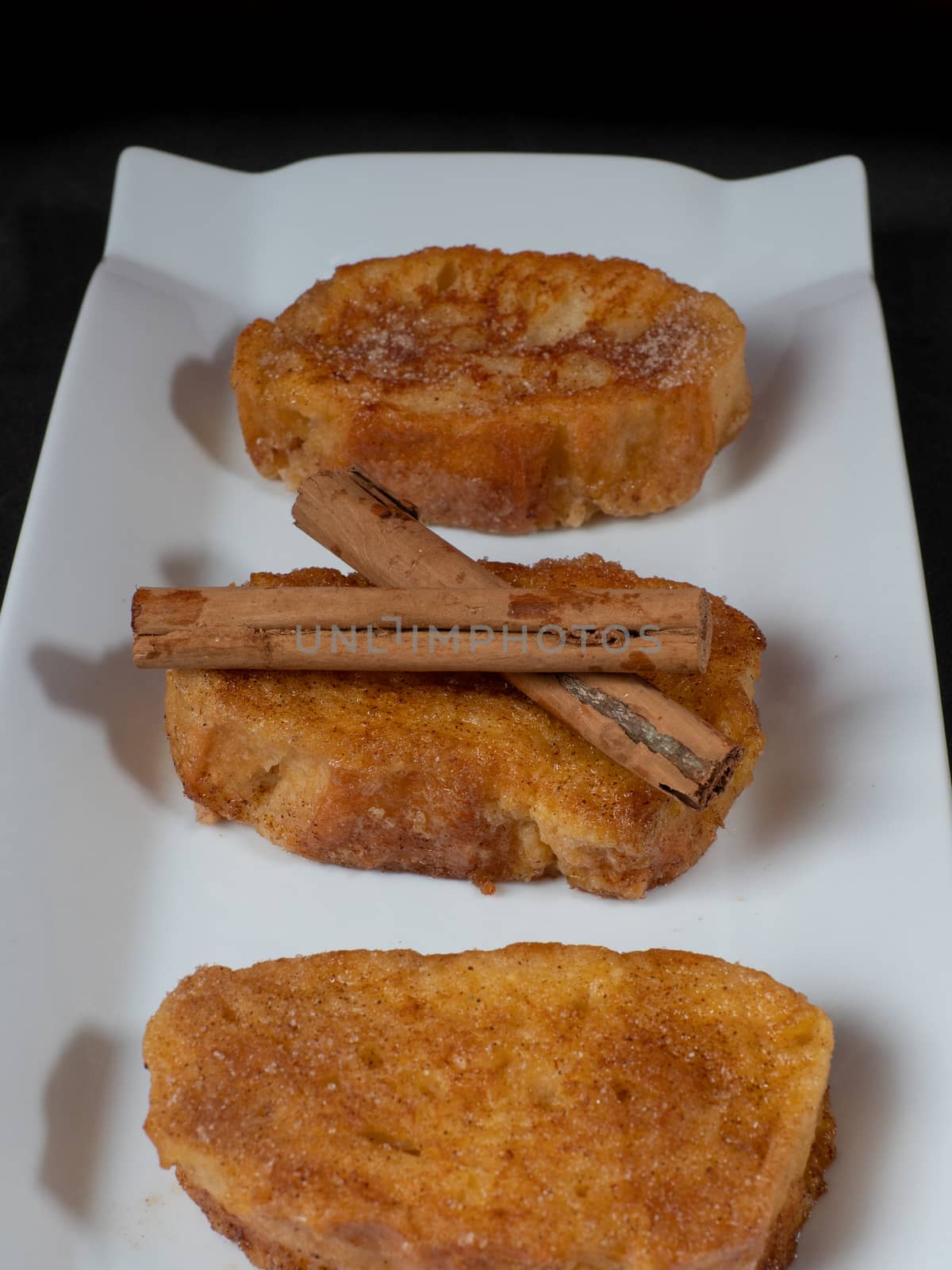 three french toast with cinnamon on white plate and dark background