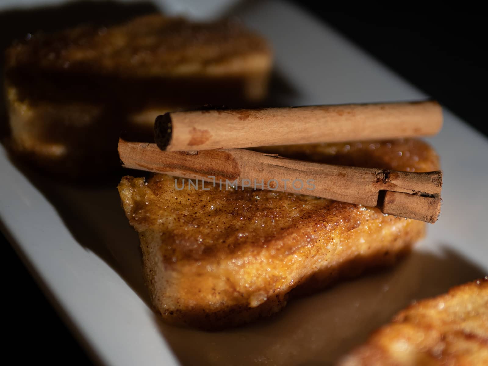 three french toast with cinnamon on white plate and dark background