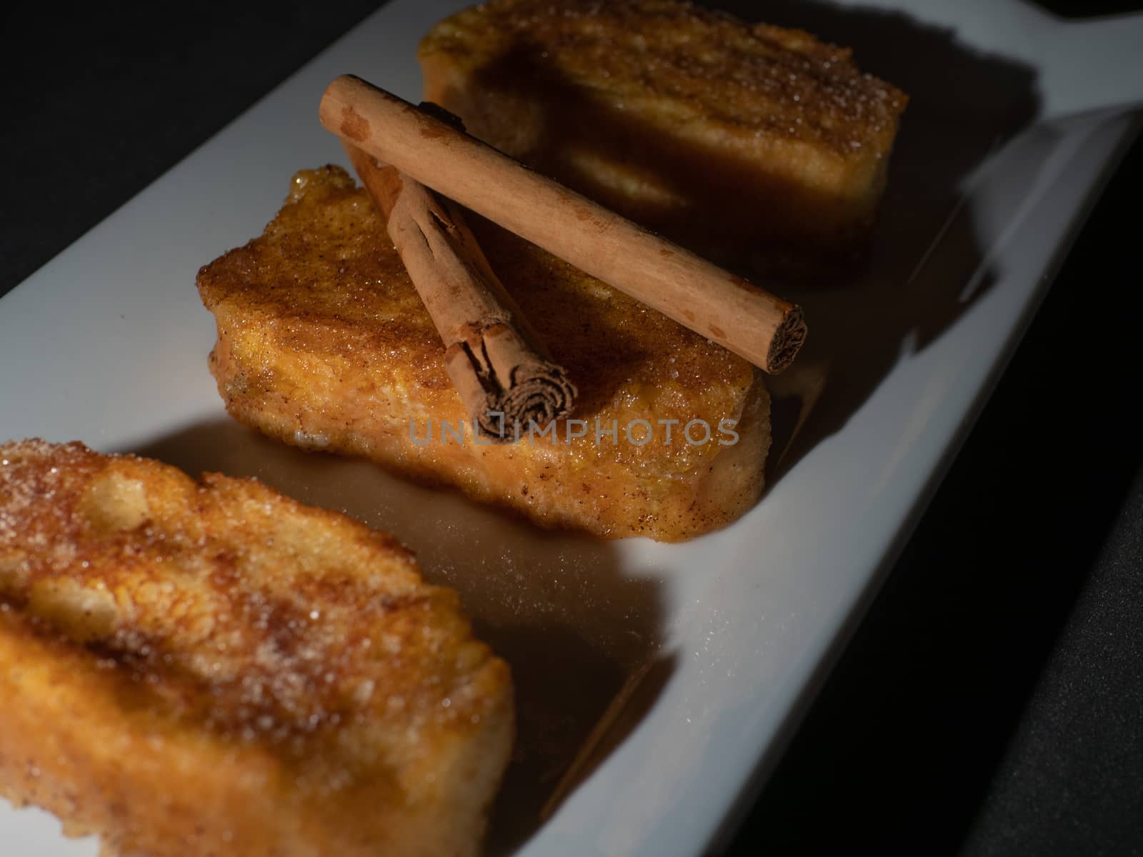 three french toast with cinnamon on white plate and dark background