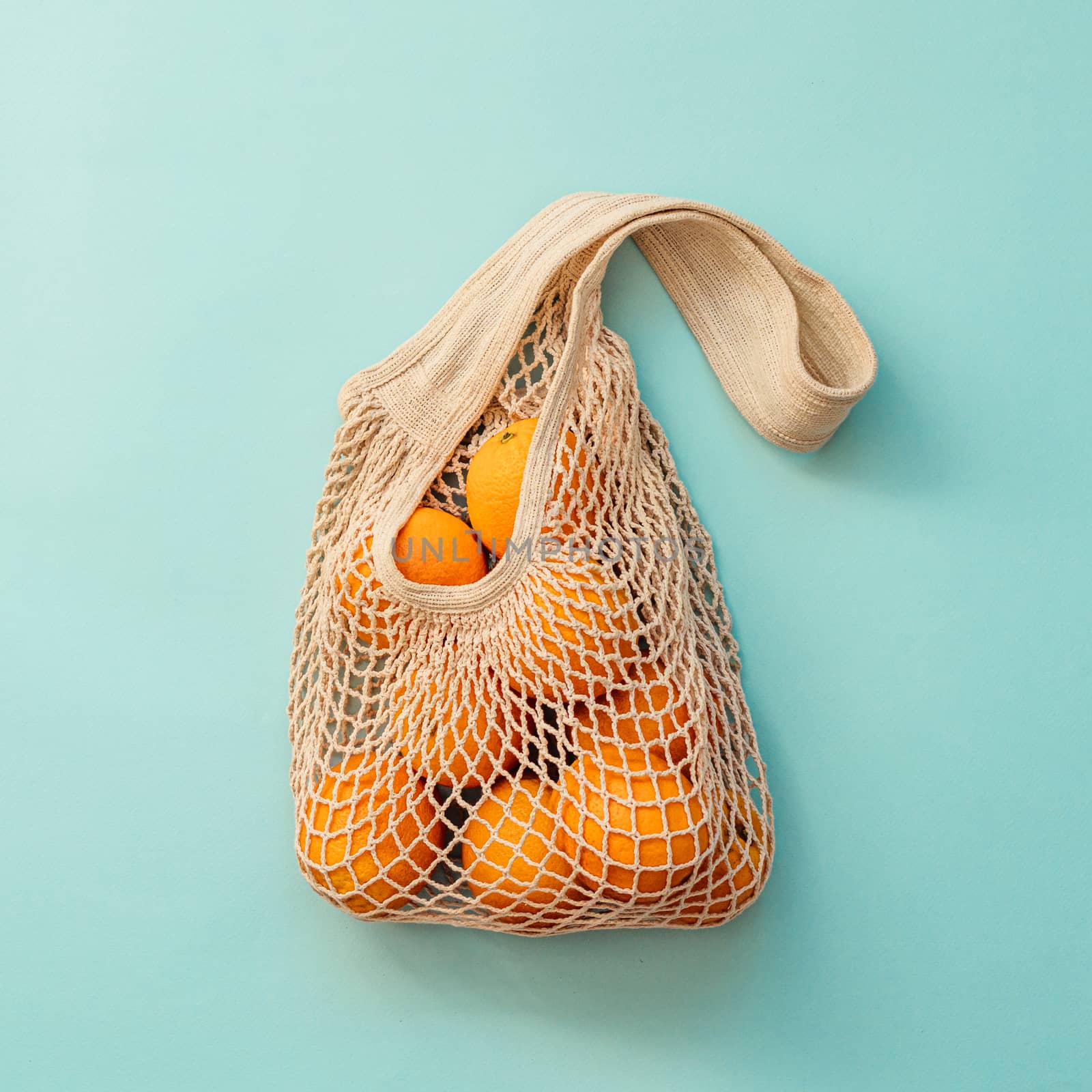 Mesh bag with fruits on blue background. Modern reusable shopping and zero waste concept. Square crop