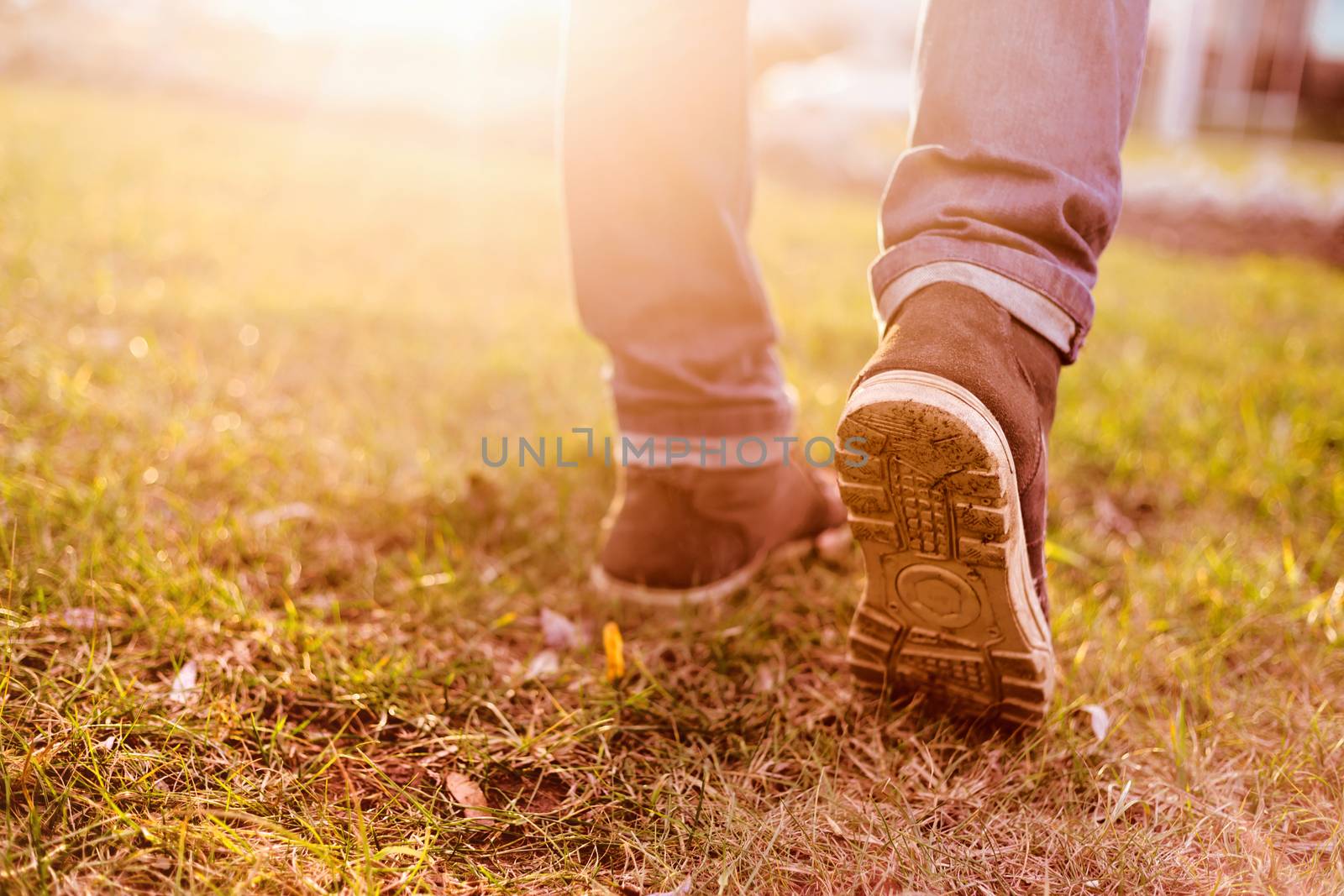 Man in shoes going on grass in front of sunlight by vladdeep