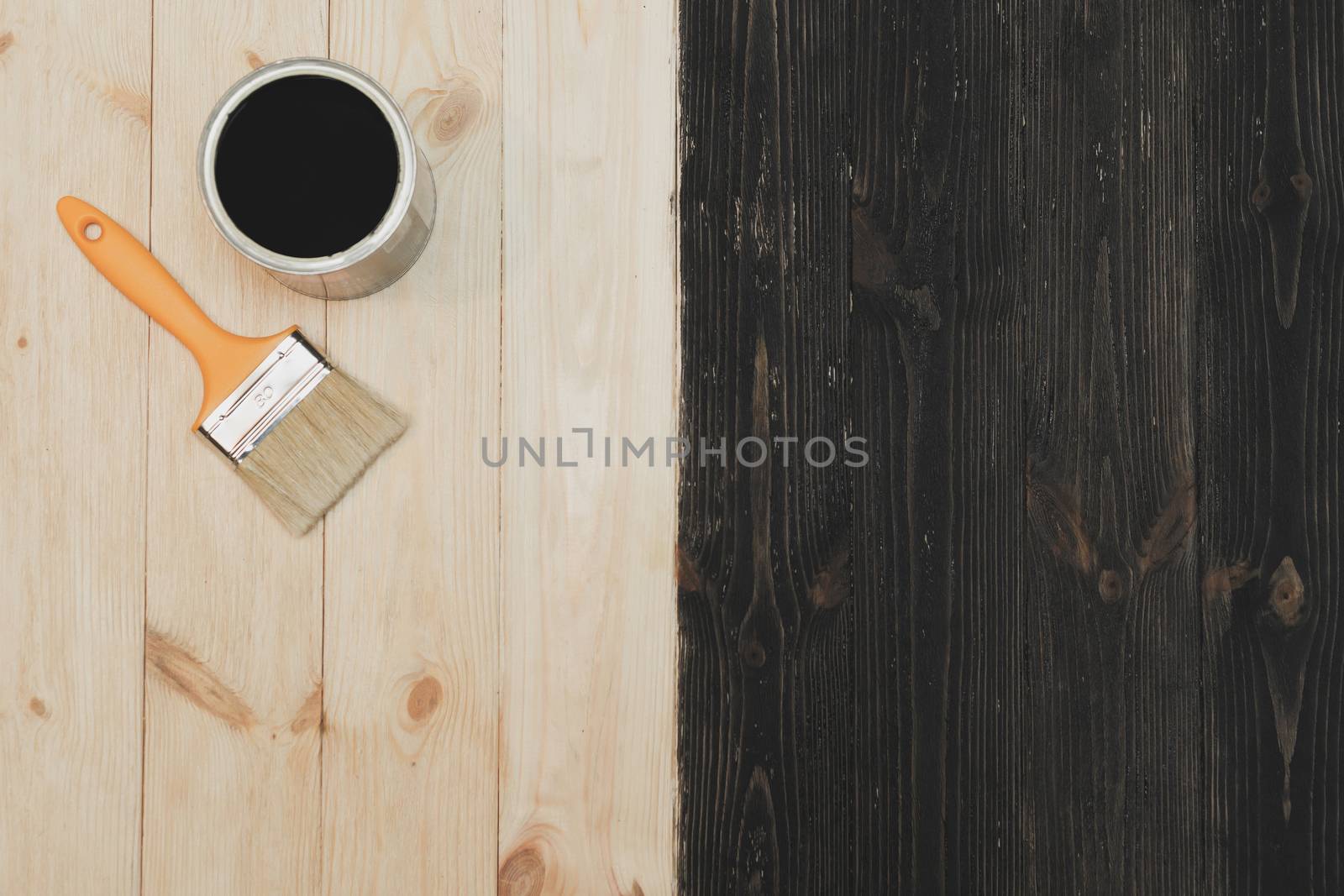 Paint brush near the can lying on wooden background. The surface is half colored with black. Top view. by vladdeep