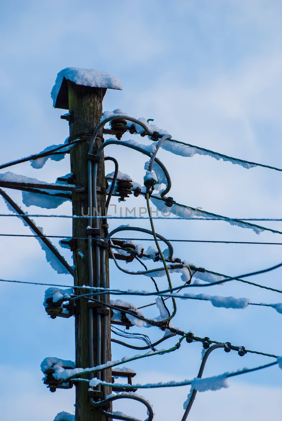 A convoluted mess of wires and cables clutter a wooden telephone pole and street lamp UK by paddythegolfer