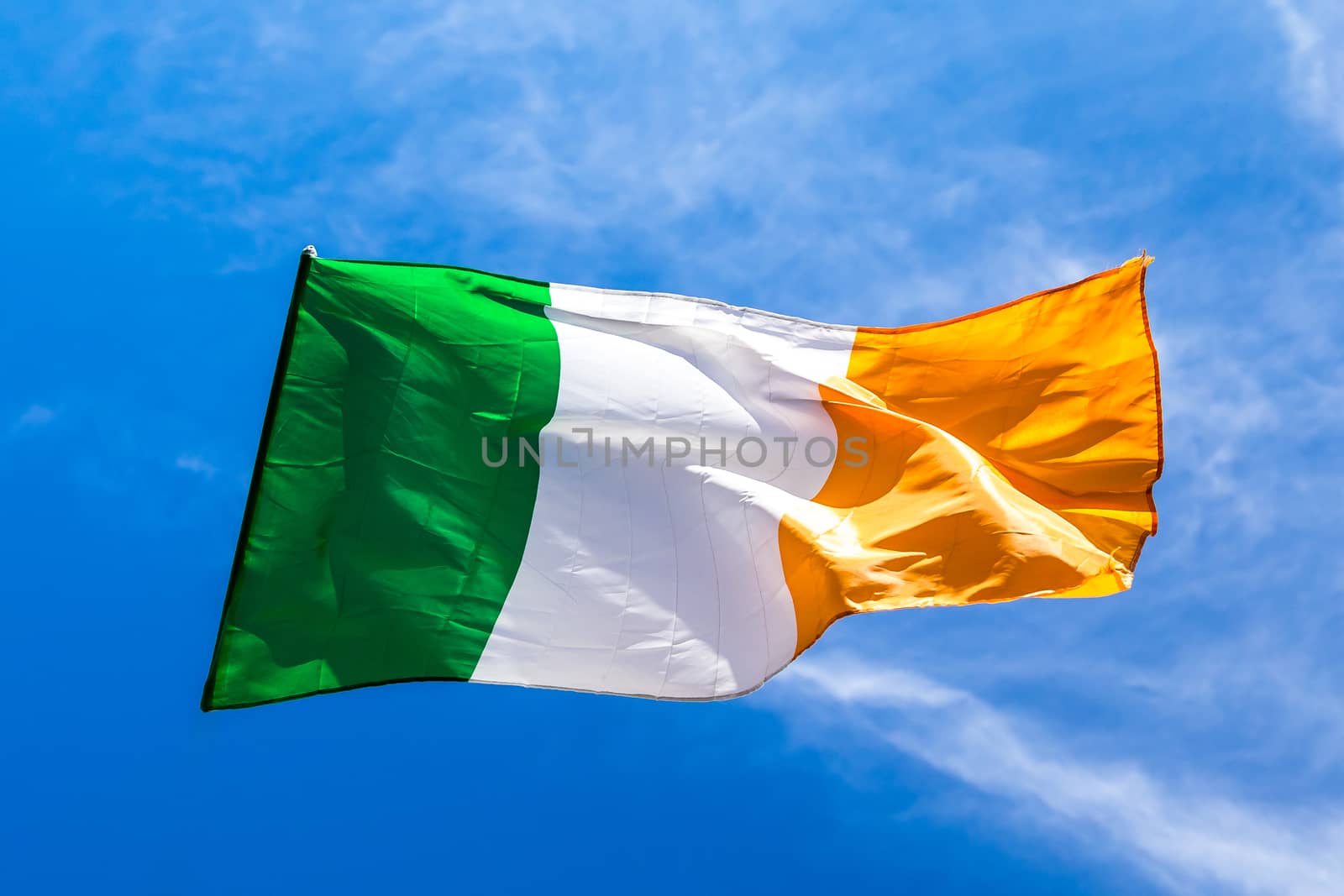 Irish flag fluttering in a brisk breeze against a bright blue sky. Europe.