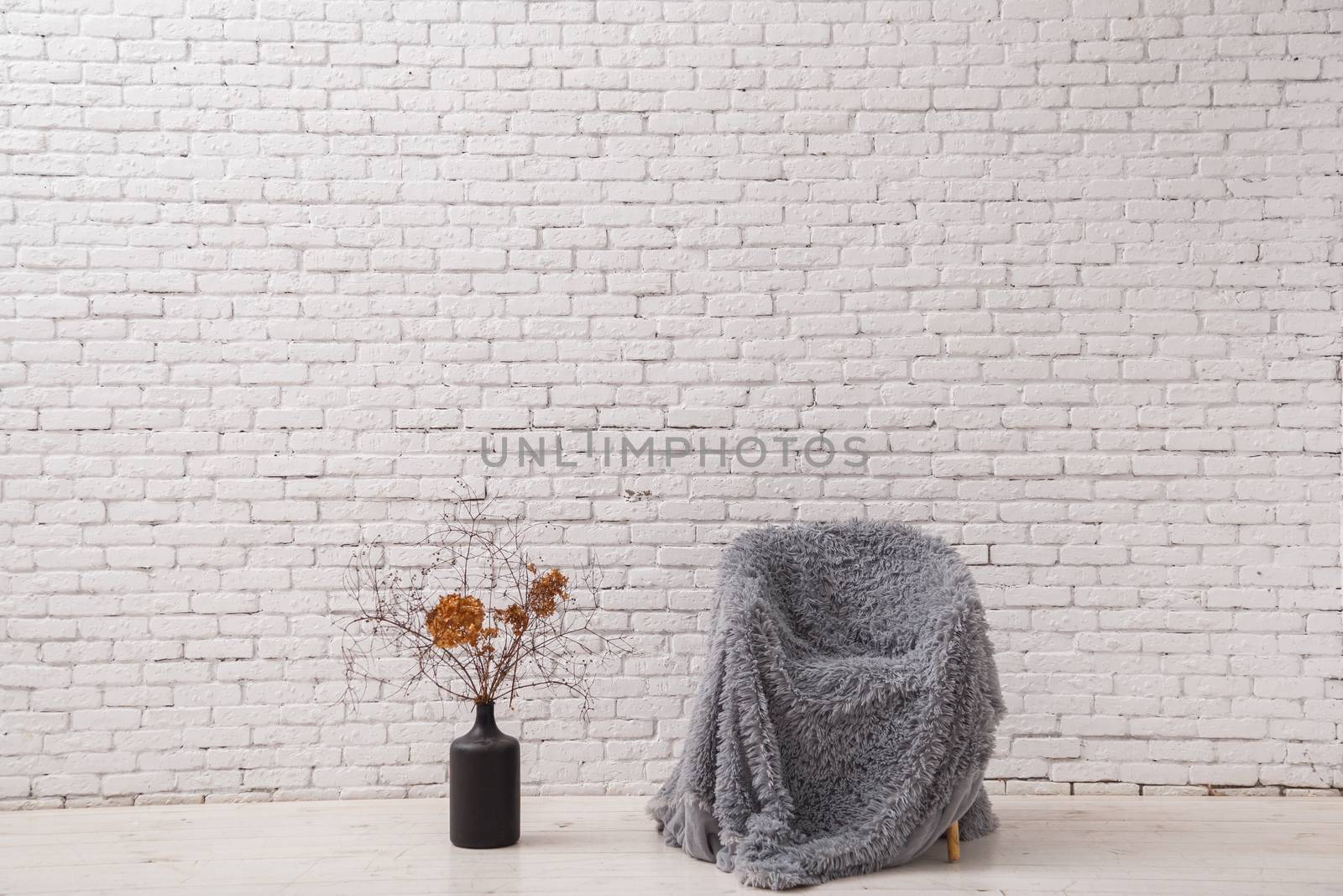 Interior in the style of minimalism. Chair and pot with dry branches against a white brick wall