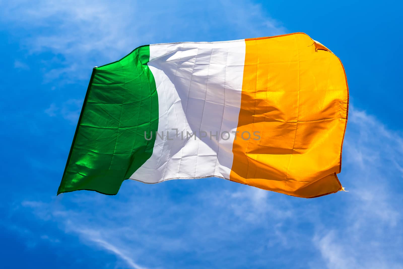 Irish flag fluttering in a brisk breeze against a bright blue sky. Europe.