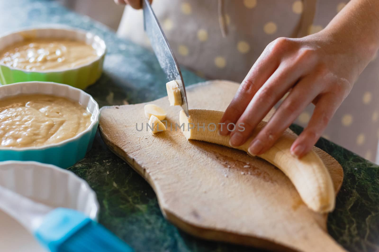 Woman cuts a banana with a knife on rude wooden board