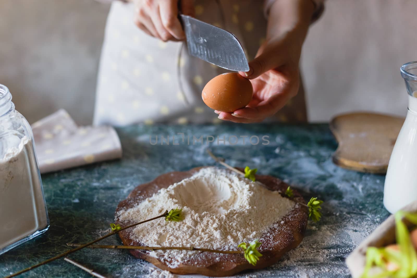 Breaking an egg with a knife into a hill of flour. Cooking baking. Female hand baker close-up. Before the crack