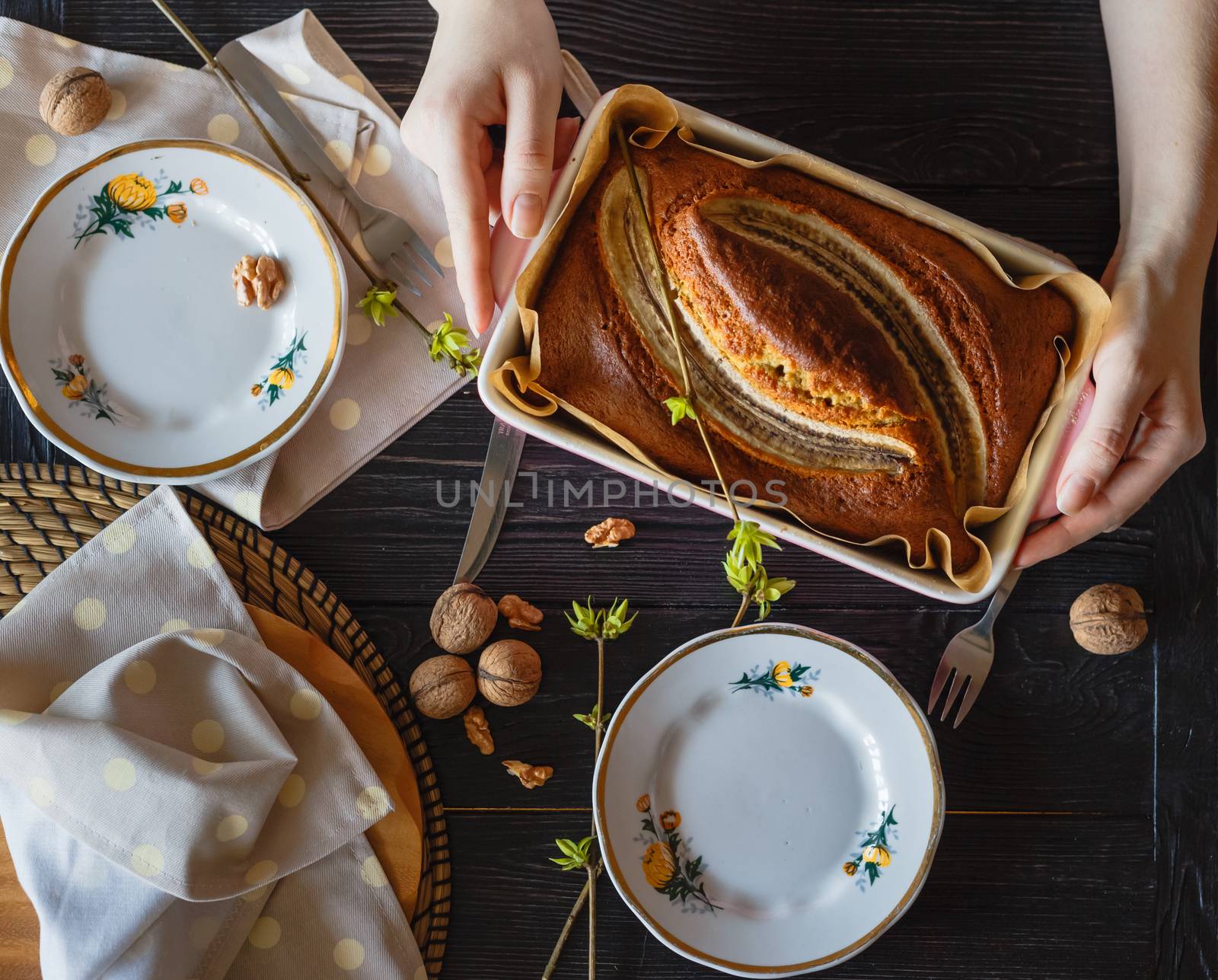 Baker puts on the table with utensils a pan with banana pie.