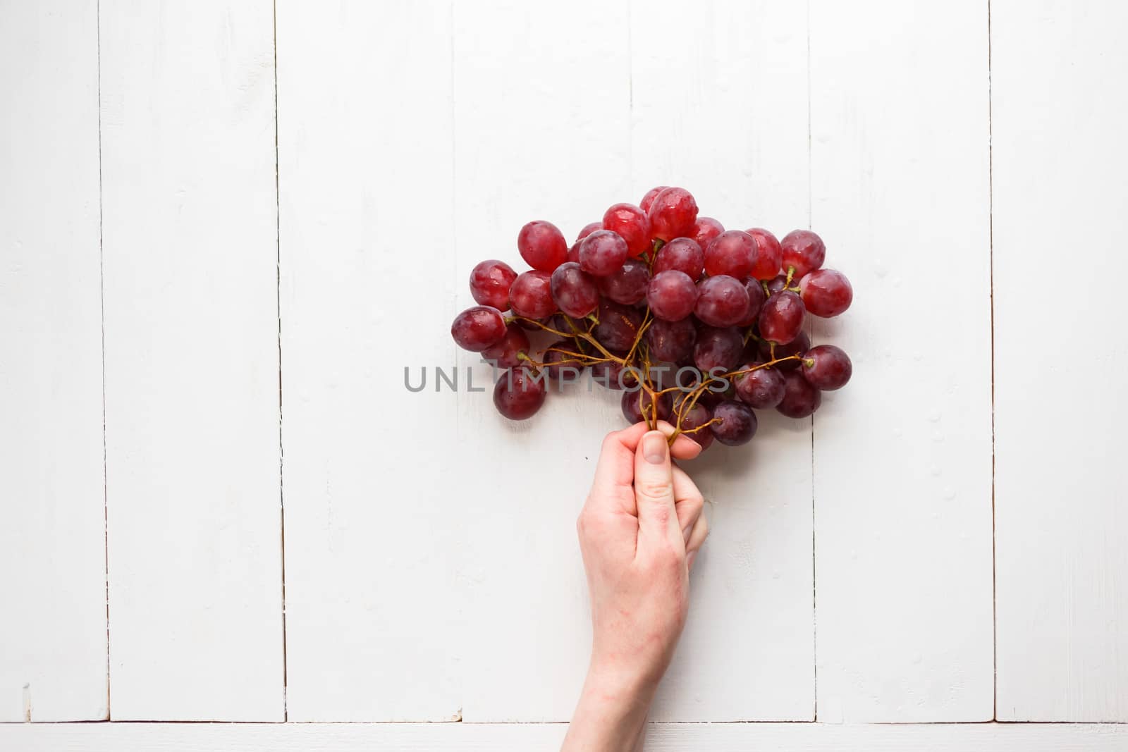 The girl's hand holds on to a bunch of red grapes on a wooden background. View from above. Grapes are like balloons