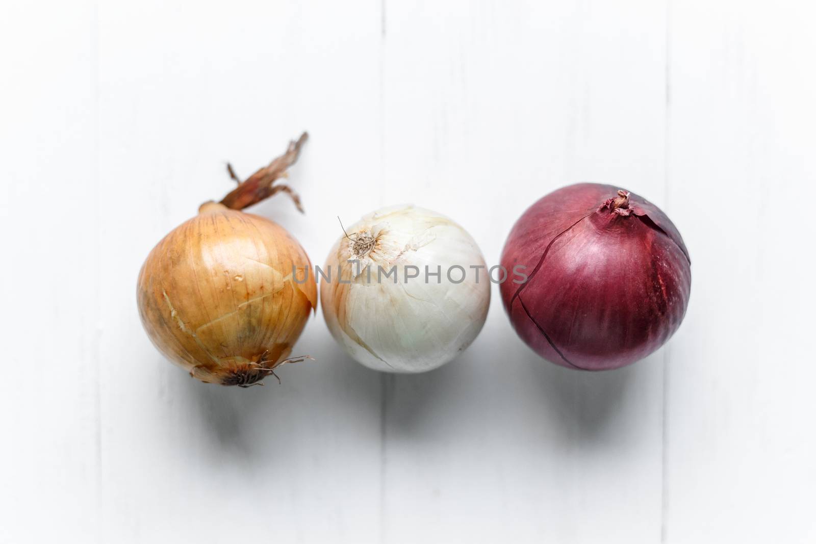 Three bulbs on a white wooden background. White onions, onions and red onions. Top view. by vladdeep