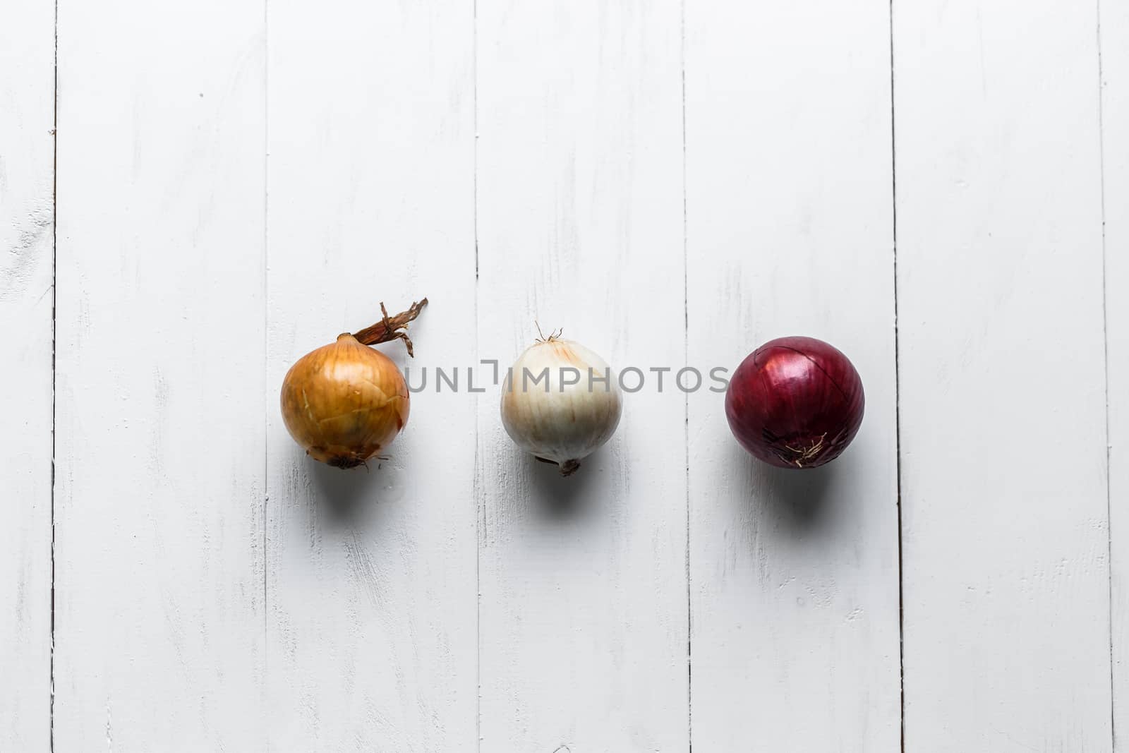 Three bulbs on a white wooden background. White onions, onions and red onions. Top view. by vladdeep