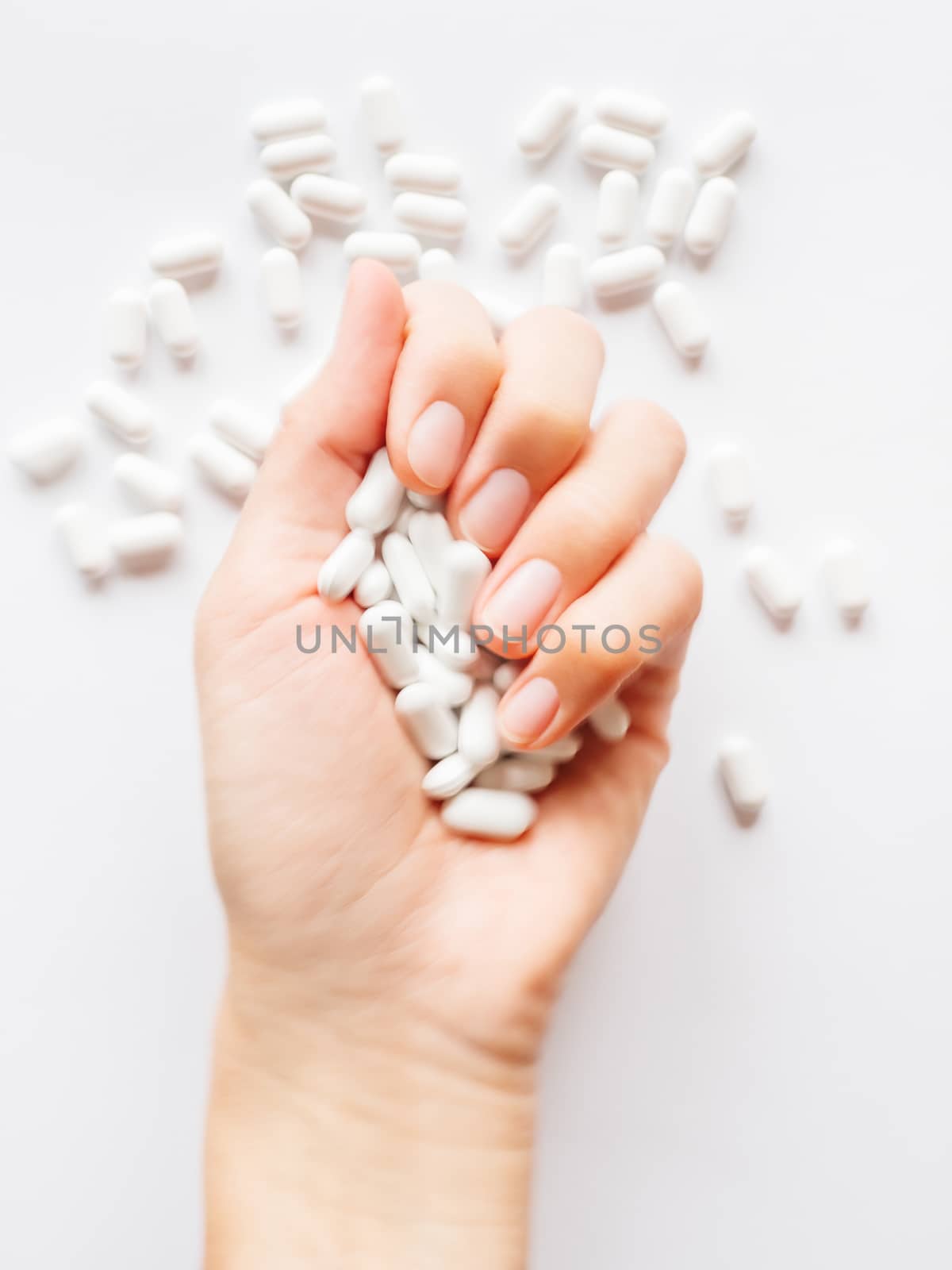 Palm hand full of white scattering pills. Woman gripes hand with capsules with medicines on light background. Flat lay, top view.