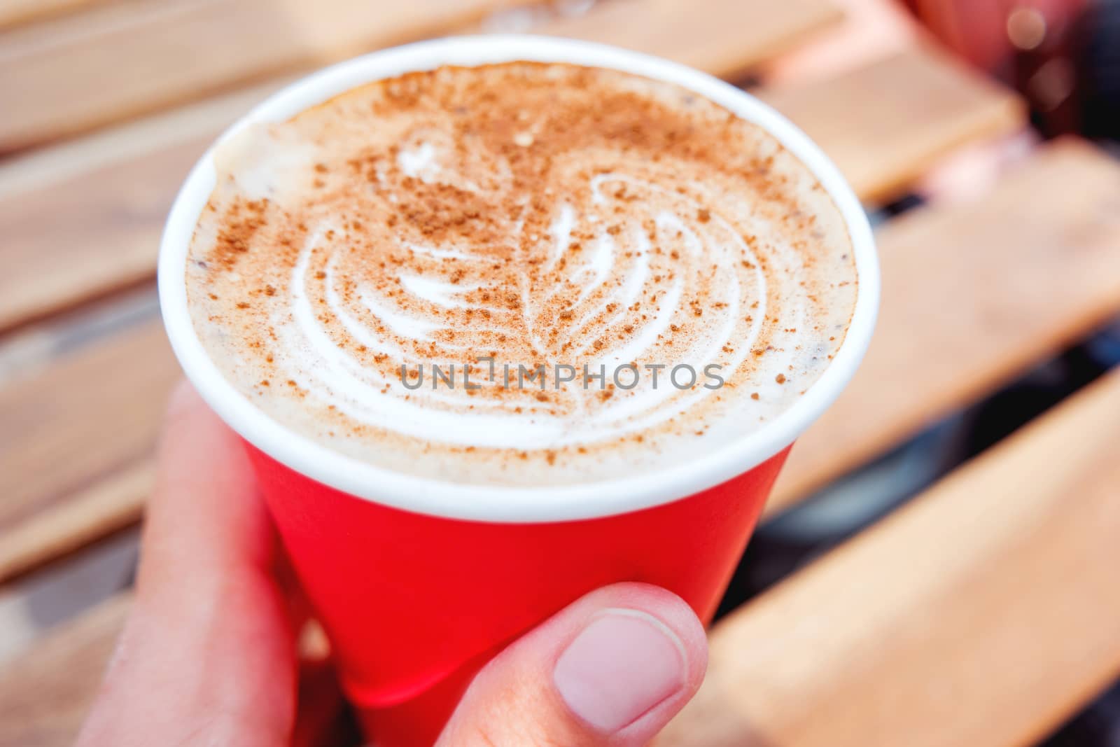Woman holding a paper cup with coffee. Coffee to go. Tasty hot beverage on wooden table in sunny day. Outdoors meal. Close up.