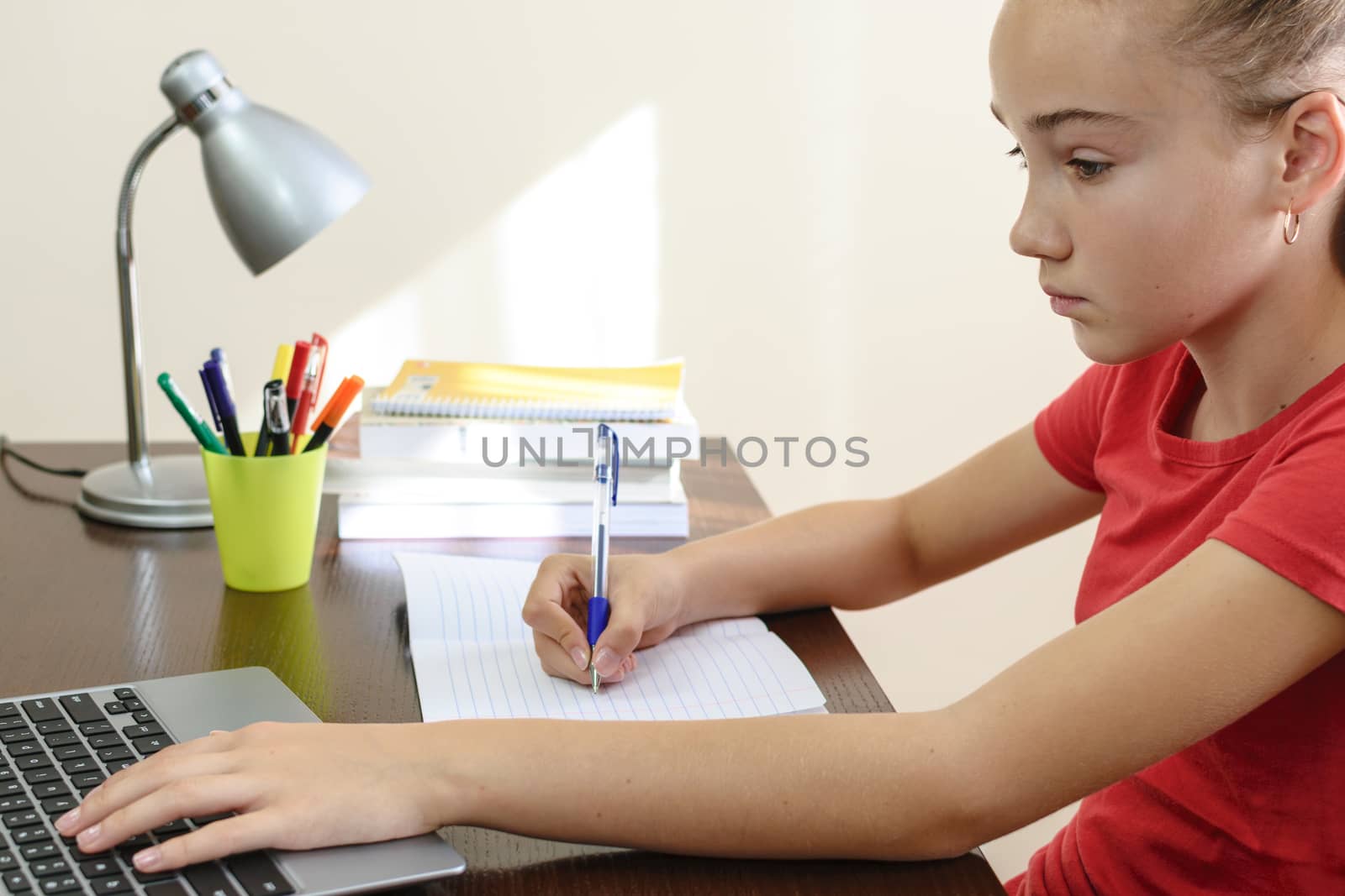 Young female student doing homework on a laptop in her room.