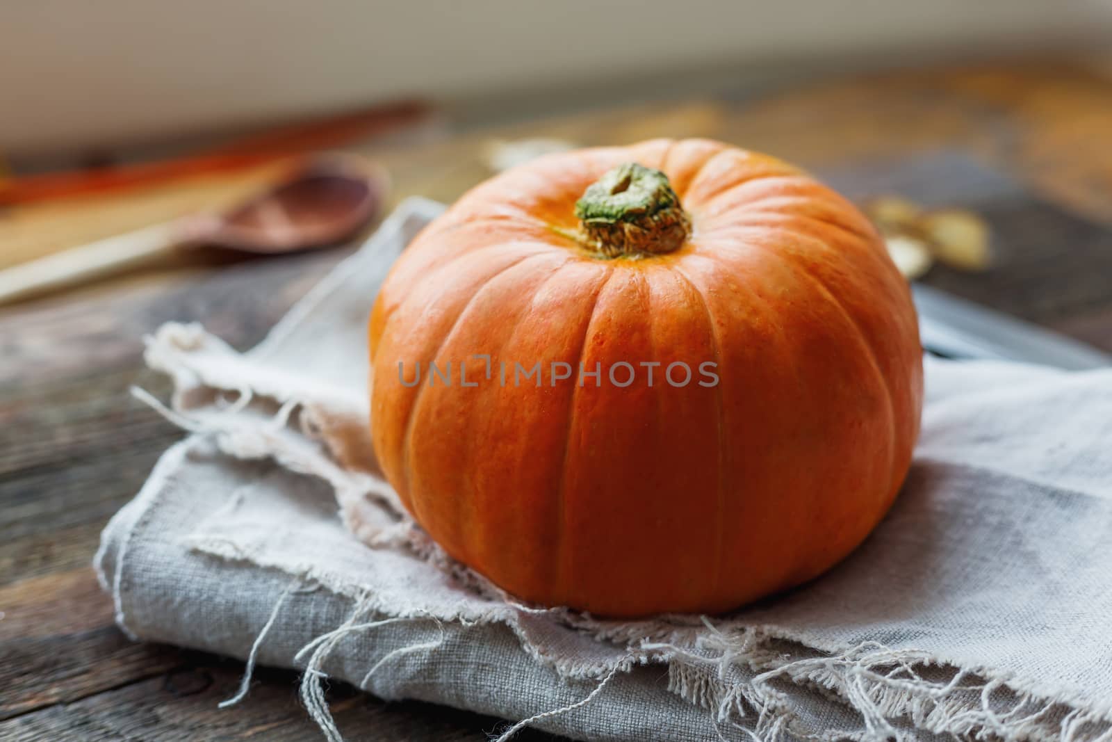 Fresh orange pumpkin on wooden table. Homespun napkin and rustic cutlery on background.