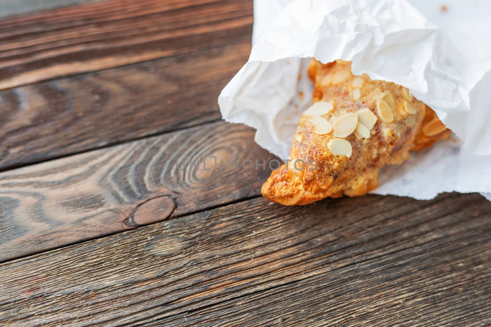 Tasty croissant in white paper bag on table. Rustic wooden background with sweet dessert.